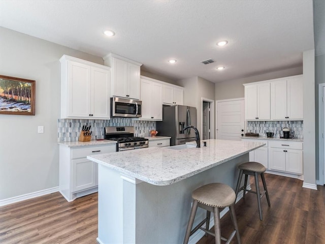 kitchen with white cabinetry, stainless steel appliances, sink, a kitchen island with sink, and light stone counters