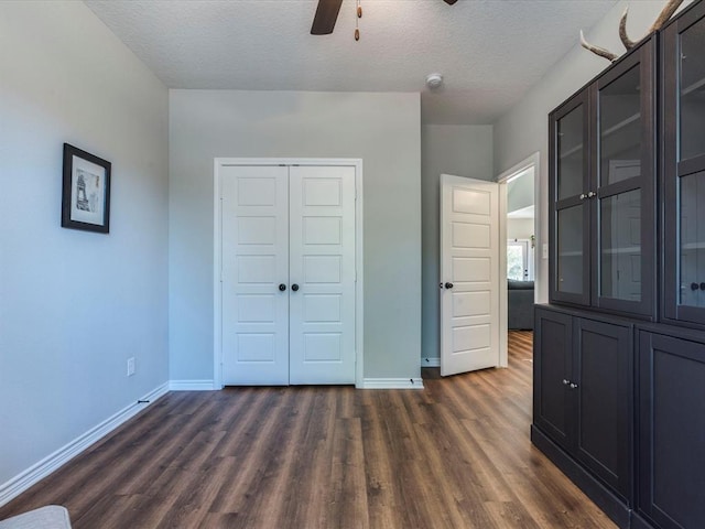 unfurnished bedroom with ceiling fan, a closet, dark hardwood / wood-style floors, and a textured ceiling