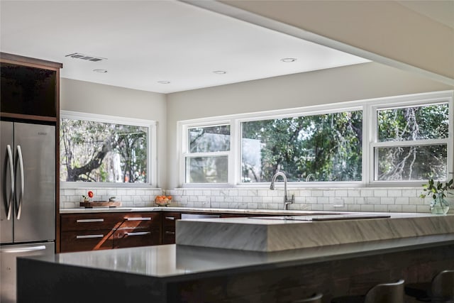 kitchen featuring tasteful backsplash, a wealth of natural light, dark brown cabinets, and stainless steel refrigerator