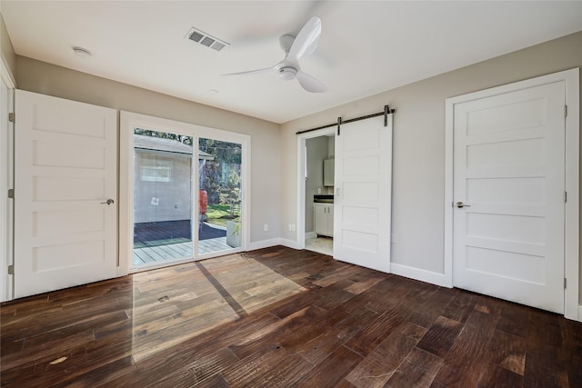 unfurnished bedroom with dark wood-type flooring, access to outside, ceiling fan, ensuite bathroom, and a barn door