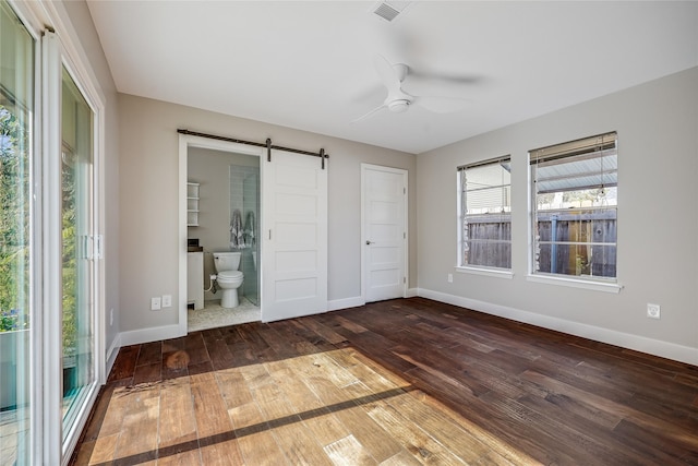 unfurnished bedroom featuring ensuite bathroom, a barn door, hardwood / wood-style flooring, ceiling fan, and a closet