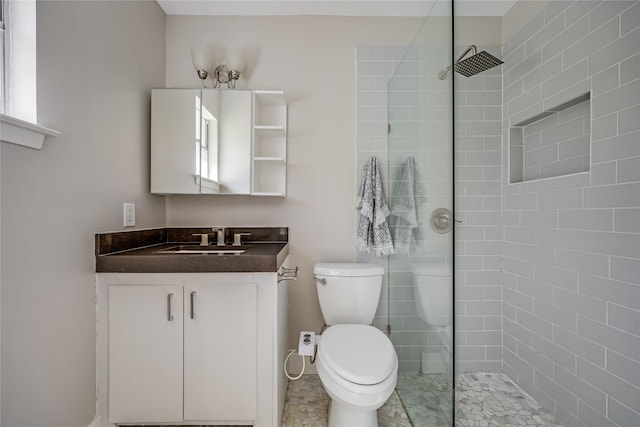 bathroom featuring toilet, tiled shower, and vanity