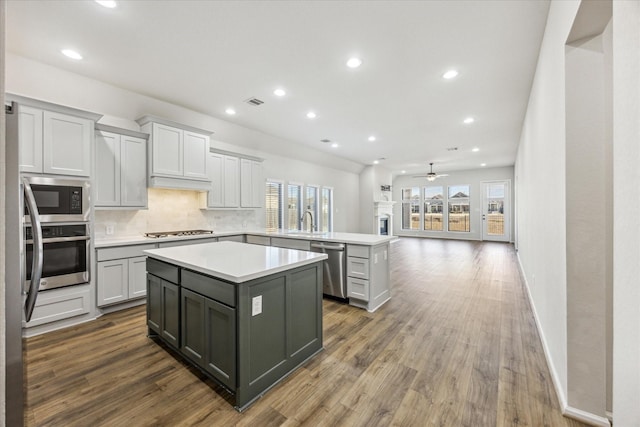 kitchen with appliances with stainless steel finishes, a center island, dark hardwood / wood-style flooring, tasteful backsplash, and ceiling fan