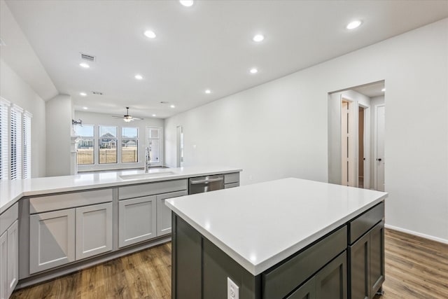 kitchen with gray cabinets, a kitchen island, stainless steel dishwasher, sink, and dark hardwood / wood-style flooring