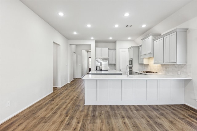 kitchen with decorative backsplash, appliances with stainless steel finishes, dark hardwood / wood-style floors, and kitchen peninsula