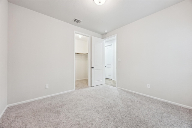 unfurnished bedroom with a walk in closet, a closet, and light colored carpet