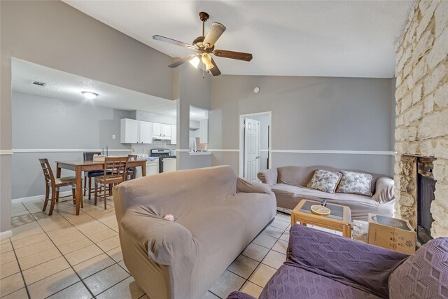 living room featuring vaulted ceiling, ceiling fan, light tile patterned floors, and a stone fireplace