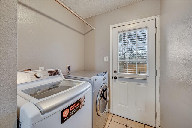 clothes washing area featuring washing machine and dryer, light tile patterned flooring, and a textured ceiling