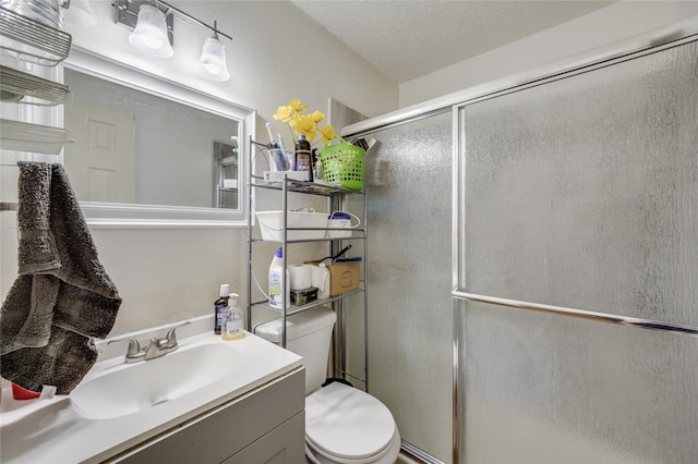 bathroom featuring a shower with shower door, vanity, toilet, and a textured ceiling