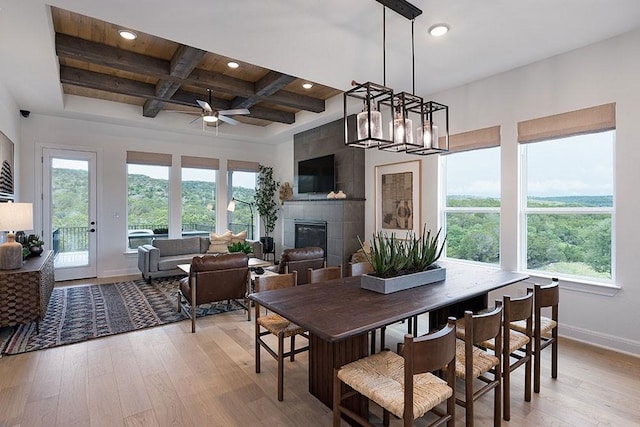 dining area featuring light hardwood / wood-style floors, beam ceiling, coffered ceiling, a tiled fireplace, and ceiling fan with notable chandelier