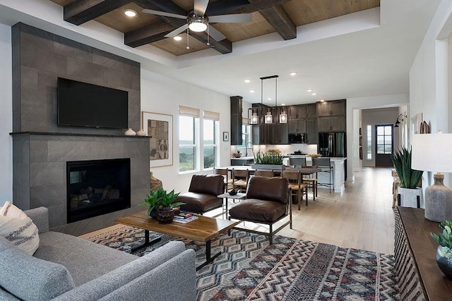 living room with beamed ceiling, a fireplace, ceiling fan, wooden ceiling, and light hardwood / wood-style flooring