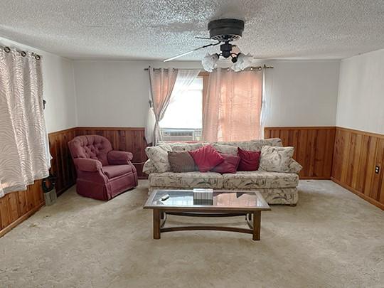 carpeted living room featuring ceiling fan, a textured ceiling, and wooden walls