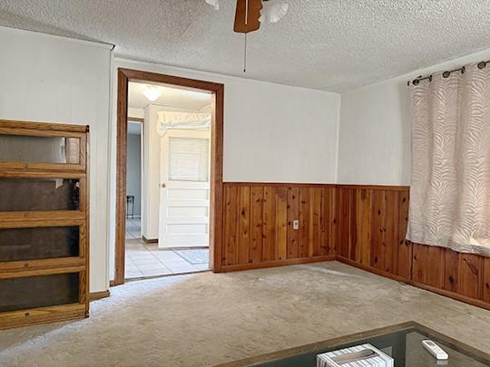 carpeted empty room with a textured ceiling, ceiling fan, and wood walls