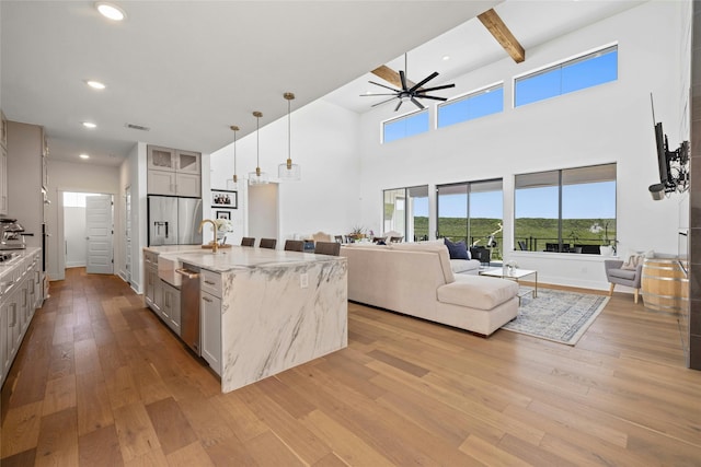 kitchen with pendant lighting, beam ceiling, a kitchen island with sink, stainless steel appliances, and light stone counters