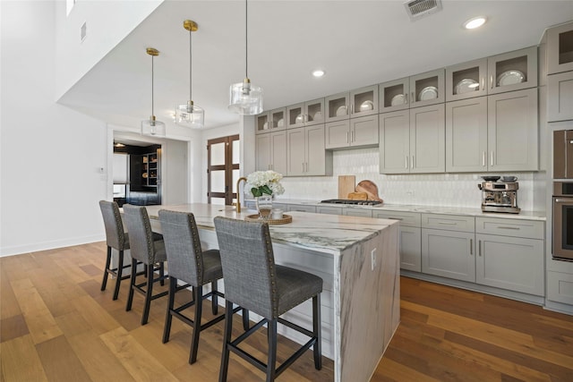 kitchen featuring light wood-type flooring, appliances with stainless steel finishes, a center island with sink, and light stone countertops