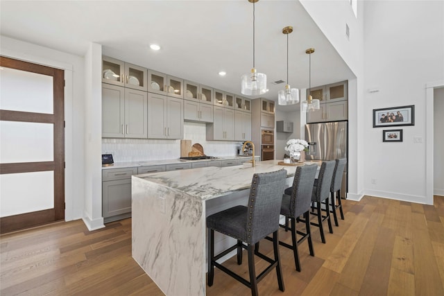 kitchen featuring appliances with stainless steel finishes, decorative light fixtures, gray cabinetry, light stone counters, and a center island with sink