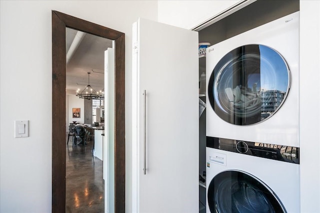 clothes washing area featuring a chandelier and stacked washer / drying machine