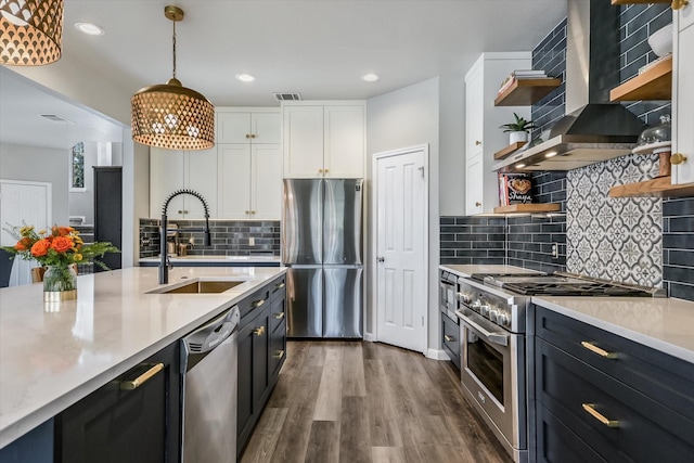 kitchen with white cabinets, appliances with stainless steel finishes, wall chimney exhaust hood, decorative light fixtures, and sink