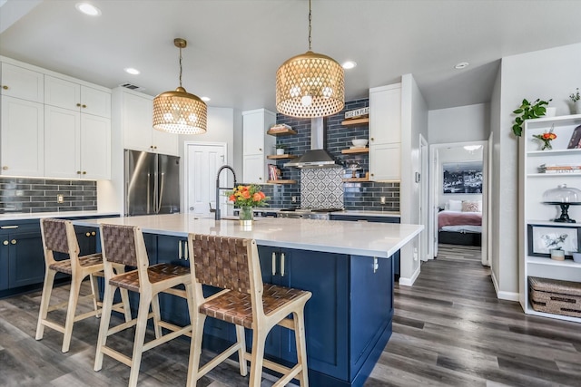 kitchen with stainless steel fridge, a kitchen island with sink, hanging light fixtures, white cabinets, and a breakfast bar