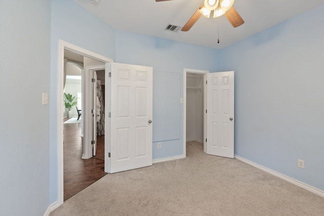 unfurnished bedroom featuring ceiling fan, a walk in closet, a closet, and light colored carpet