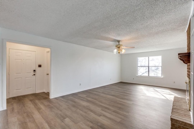 unfurnished living room featuring ceiling fan, a textured ceiling, hardwood / wood-style flooring, and a fireplace