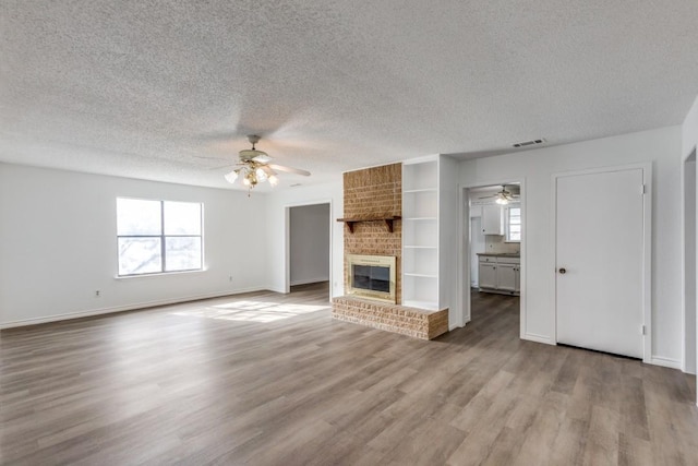 unfurnished living room with light hardwood / wood-style floors, ceiling fan, a fireplace, a textured ceiling, and built in shelves