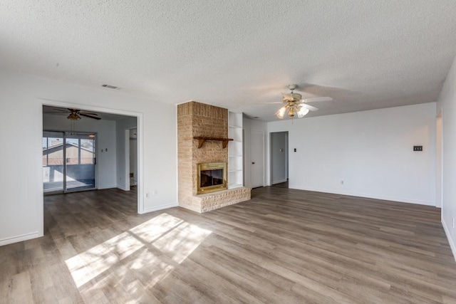 unfurnished living room with ceiling fan, a brick fireplace, a textured ceiling, and hardwood / wood-style floors