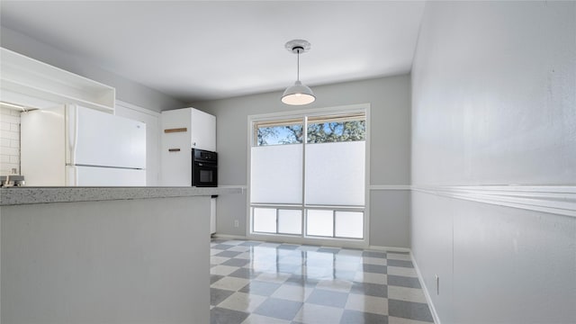 kitchen featuring white fridge, hanging light fixtures, white cabinetry, and black oven