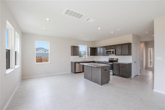 kitchen with tasteful backsplash, a kitchen island, appliances with stainless steel finishes, light tile patterned floors, and dark brown cabinets