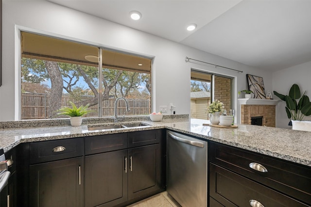 kitchen with dark brown cabinets, a fireplace, stainless steel dishwasher, light stone counters, and sink