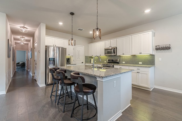 kitchen featuring a center island with sink, stainless steel appliances, stone counters, white cabinets, and sink