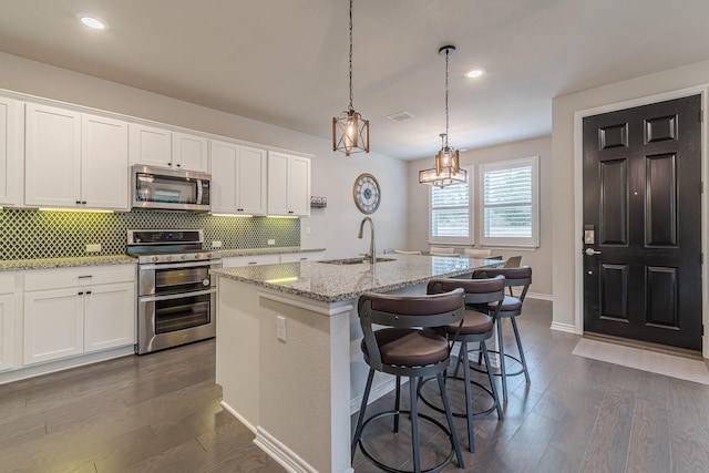 kitchen featuring white cabinets, stainless steel appliances, sink, a kitchen breakfast bar, and a kitchen island with sink