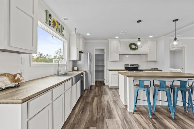 kitchen with white cabinets, decorative light fixtures, stainless steel appliances, ornamental molding, and butcher block countertops