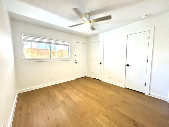 unfurnished bedroom featuring ceiling fan, a textured ceiling, light hardwood / wood-style flooring, and multiple closets