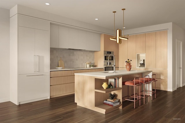 kitchen with stainless steel double oven, decorative backsplash, pendant lighting, and a center island with sink