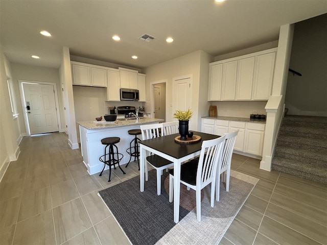 kitchen featuring an island with sink, stainless steel appliances, light tile patterned flooring, light stone countertops, and white cabinets