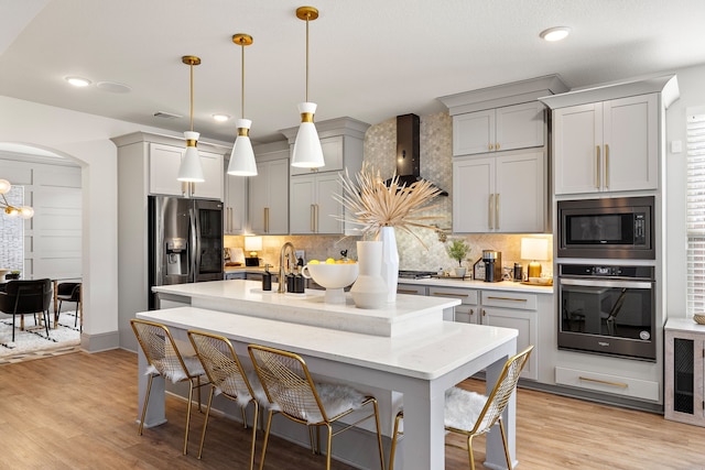 kitchen with decorative light fixtures, appliances with stainless steel finishes, wall chimney exhaust hood, and gray cabinets