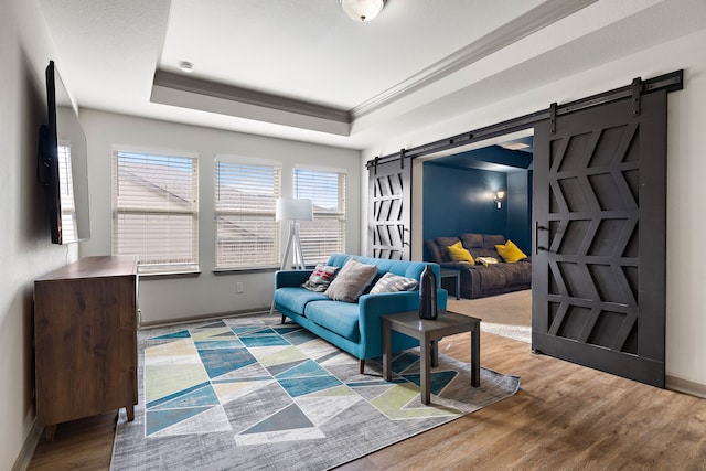 living room featuring a barn door, a tray ceiling, ornamental molding, and light hardwood / wood-style flooring