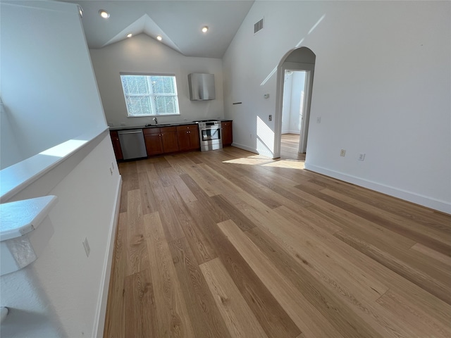 unfurnished living room with high vaulted ceiling, light wood-type flooring, and sink