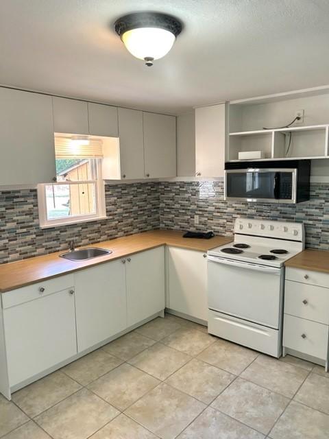 kitchen featuring wood counters, light tile patterned floors, backsplash, white range with electric cooktop, and sink