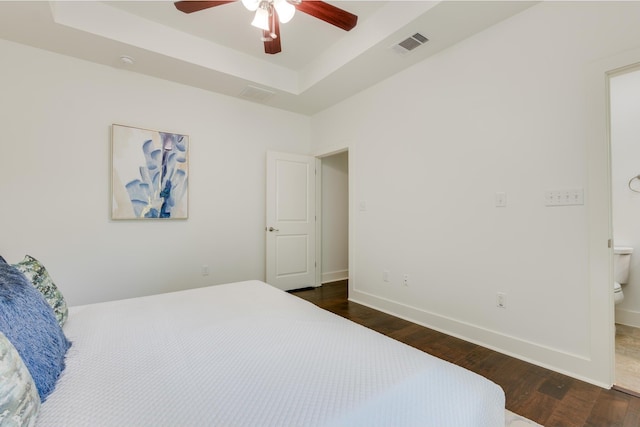 bedroom featuring ceiling fan, dark wood-type flooring, a tray ceiling, and ensuite bathroom