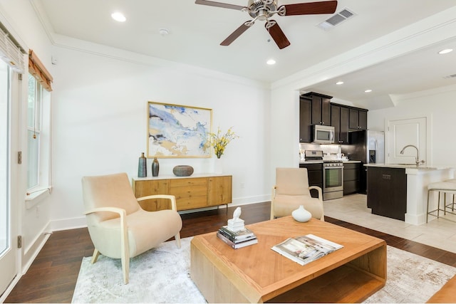 living room featuring ceiling fan, sink, light hardwood / wood-style flooring, and crown molding