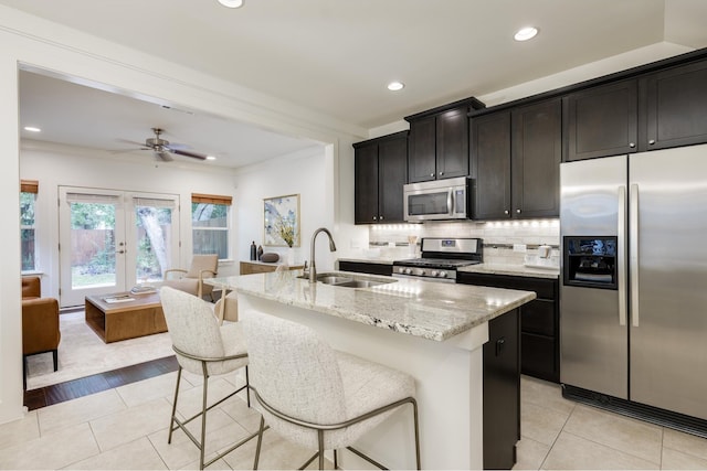 kitchen featuring sink, light stone countertops, an island with sink, stainless steel appliances, and french doors