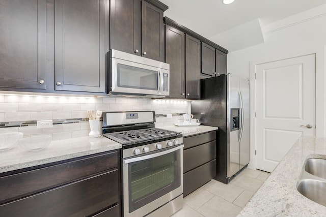 kitchen with light stone countertops, dark brown cabinetry, appliances with stainless steel finishes, tasteful backsplash, and light tile patterned floors