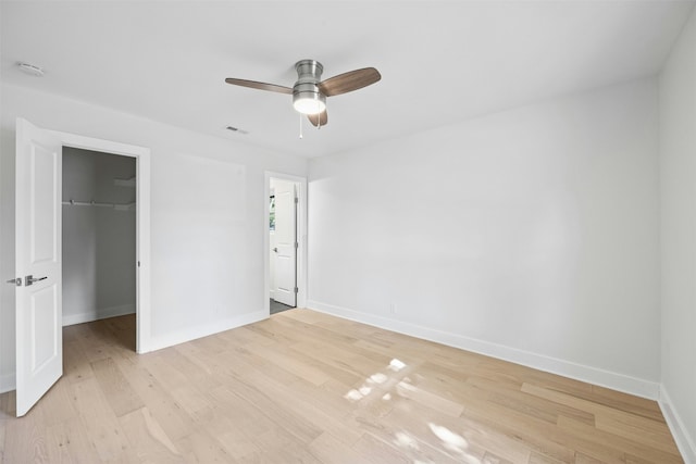 unfurnished bedroom featuring ceiling fan, a walk in closet, a closet, and light hardwood / wood-style floors