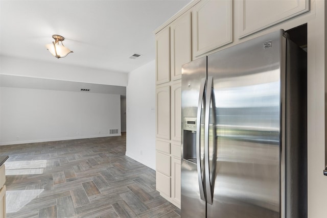 kitchen featuring cream cabinetry, stainless steel fridge, and dark parquet flooring