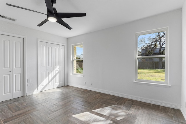 unfurnished bedroom featuring ceiling fan, multiple windows, and two closets