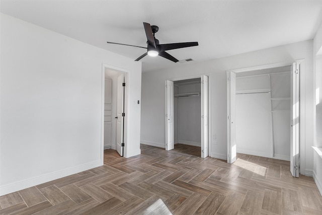 unfurnished bedroom with ceiling fan, two closets, and parquet flooring