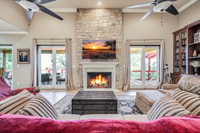 living room featuring ceiling fan, plenty of natural light, ornamental molding, and a stone fireplace