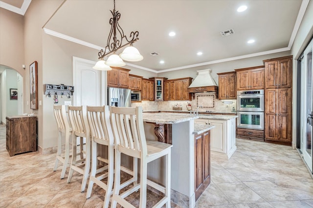 kitchen with custom exhaust hood, stainless steel appliances, decorative backsplash, light stone countertops, and a kitchen island